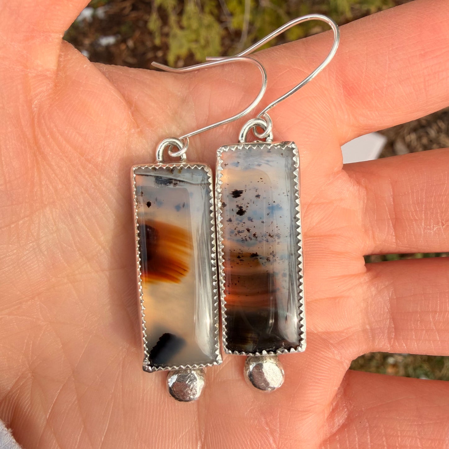 Rectangular agate earrings with silver setting held in a hand against a blurred natural background