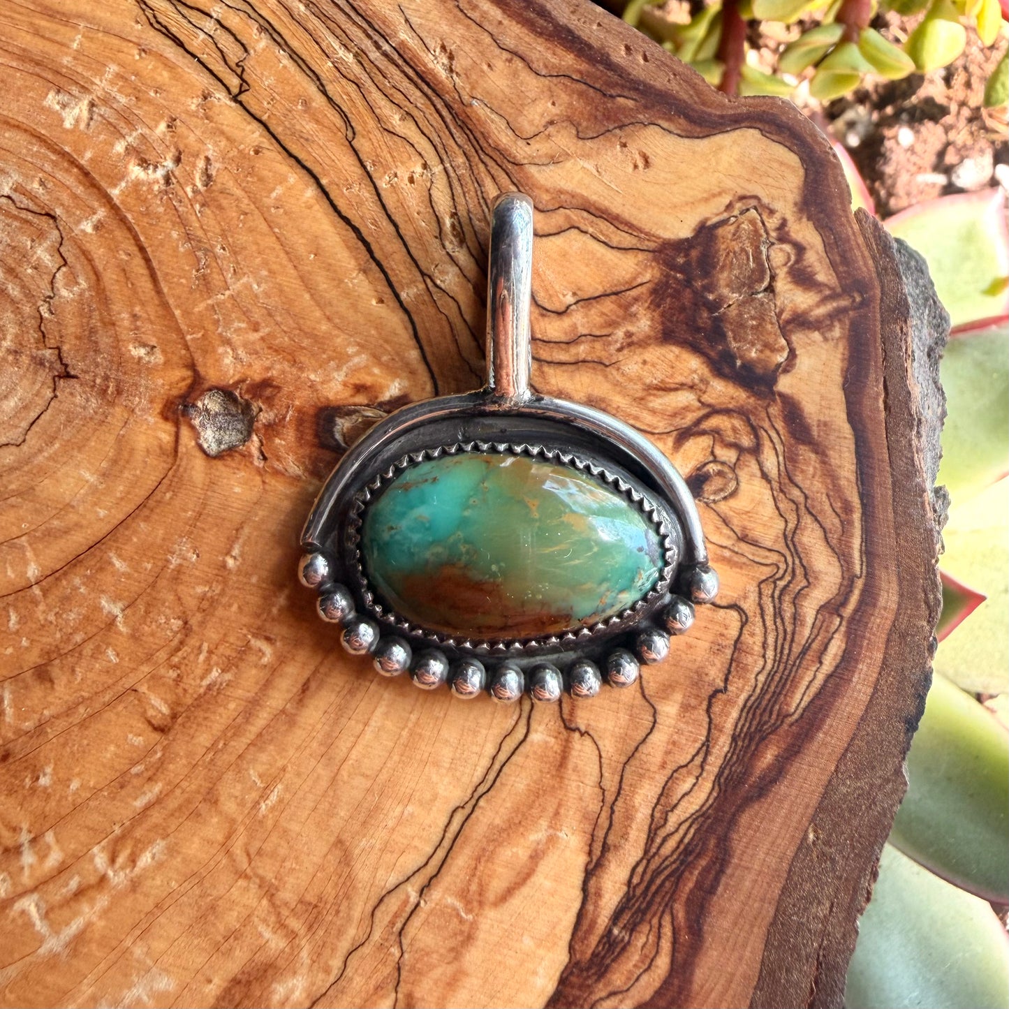 Turquoise stone pendant in silver setting on a wooden surface