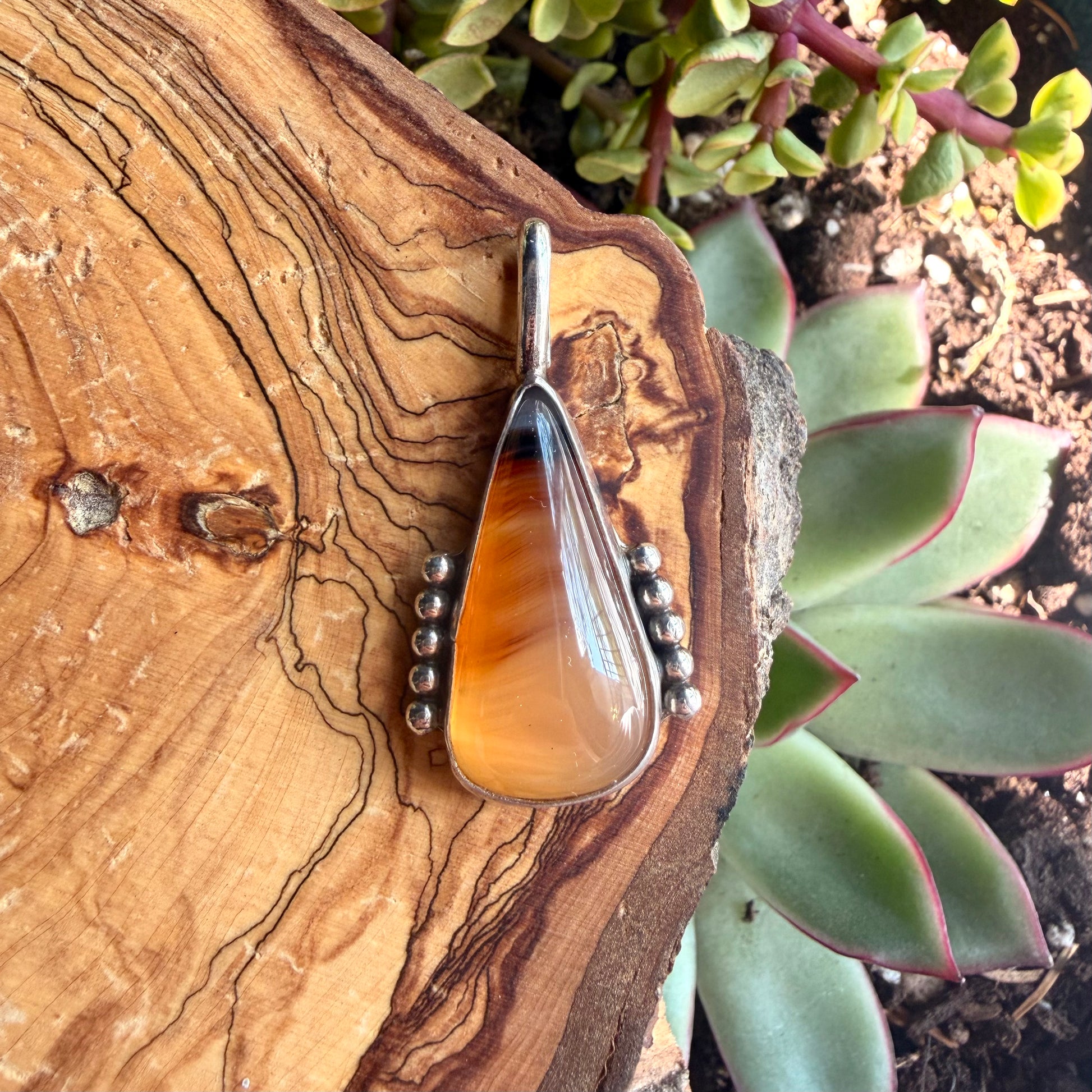 Amber pendant with silver beads on a wooden surface with succulents in the background