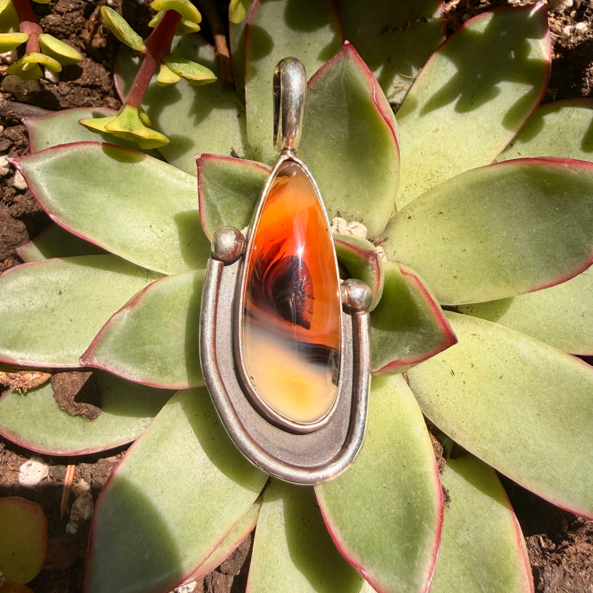 Ornate pendant with orange and black design on a succulent plant