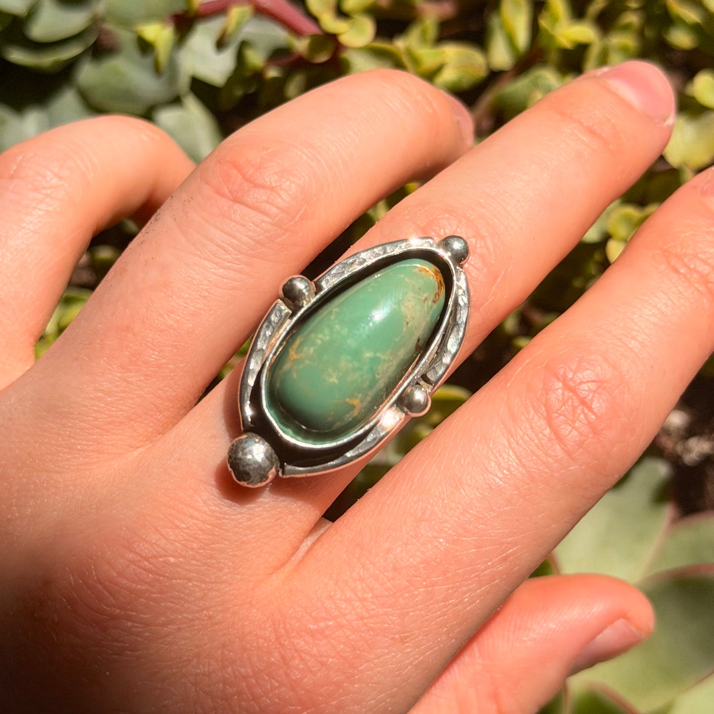 Hand wearing a silver ring with a green stone against a natural background