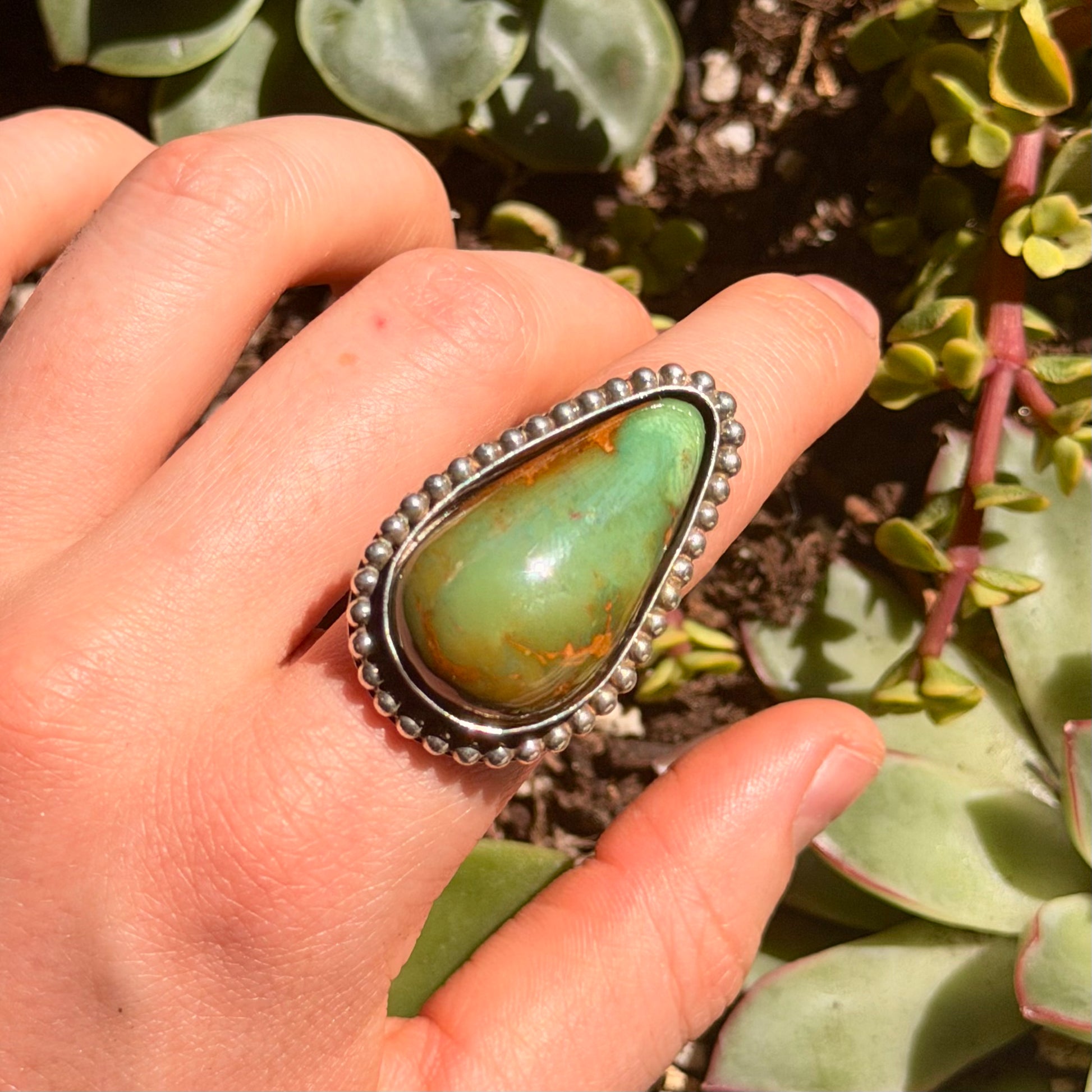 Hand wearing a ring with a green stone against a natural background