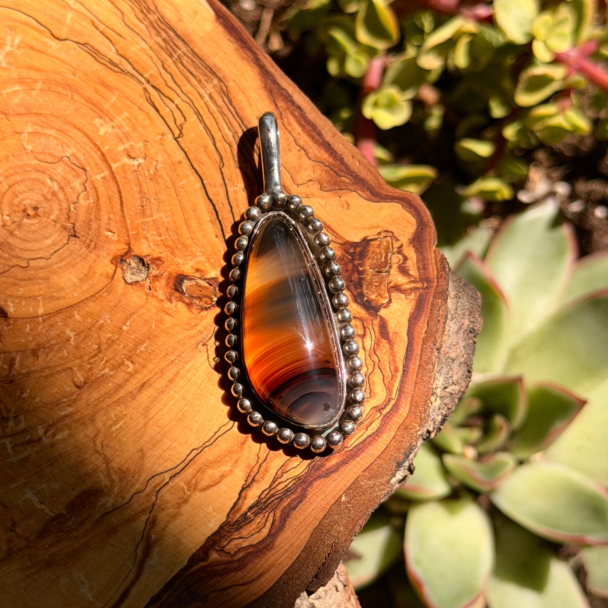 Pendant with a brown and orange pattern on a wooden surface with plants in the background