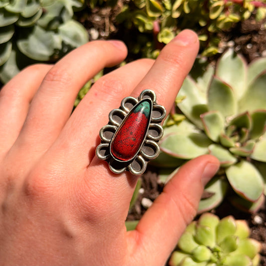 Hand wearing ring with red and green stone with blurred green background