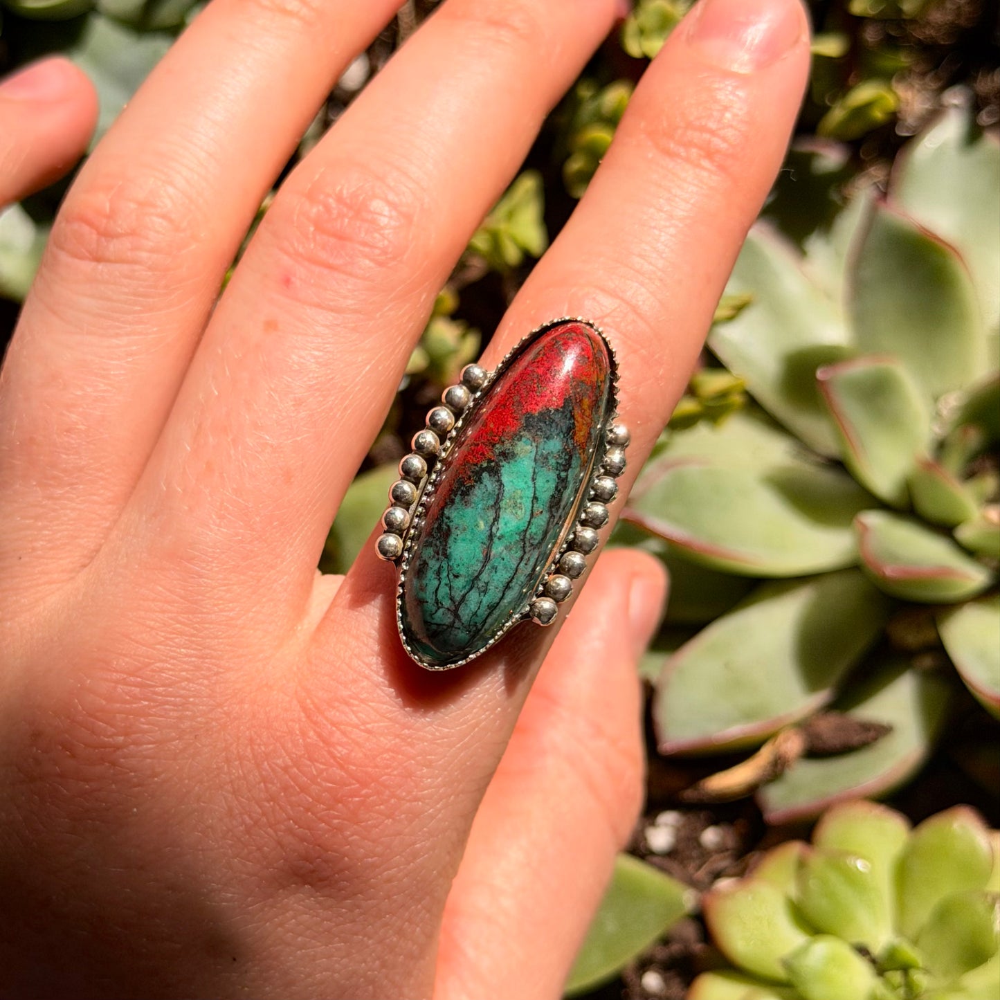 Red and green stone ring on finger with blurred green background
