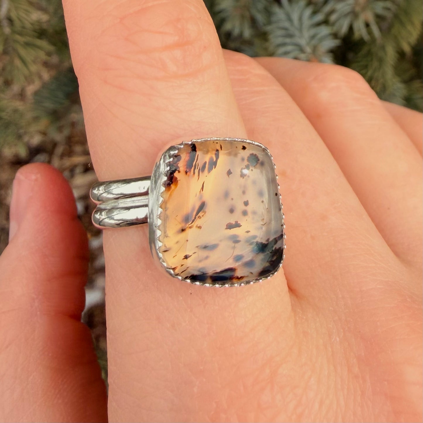 Ring with a speckled stone on a finger against a natural background