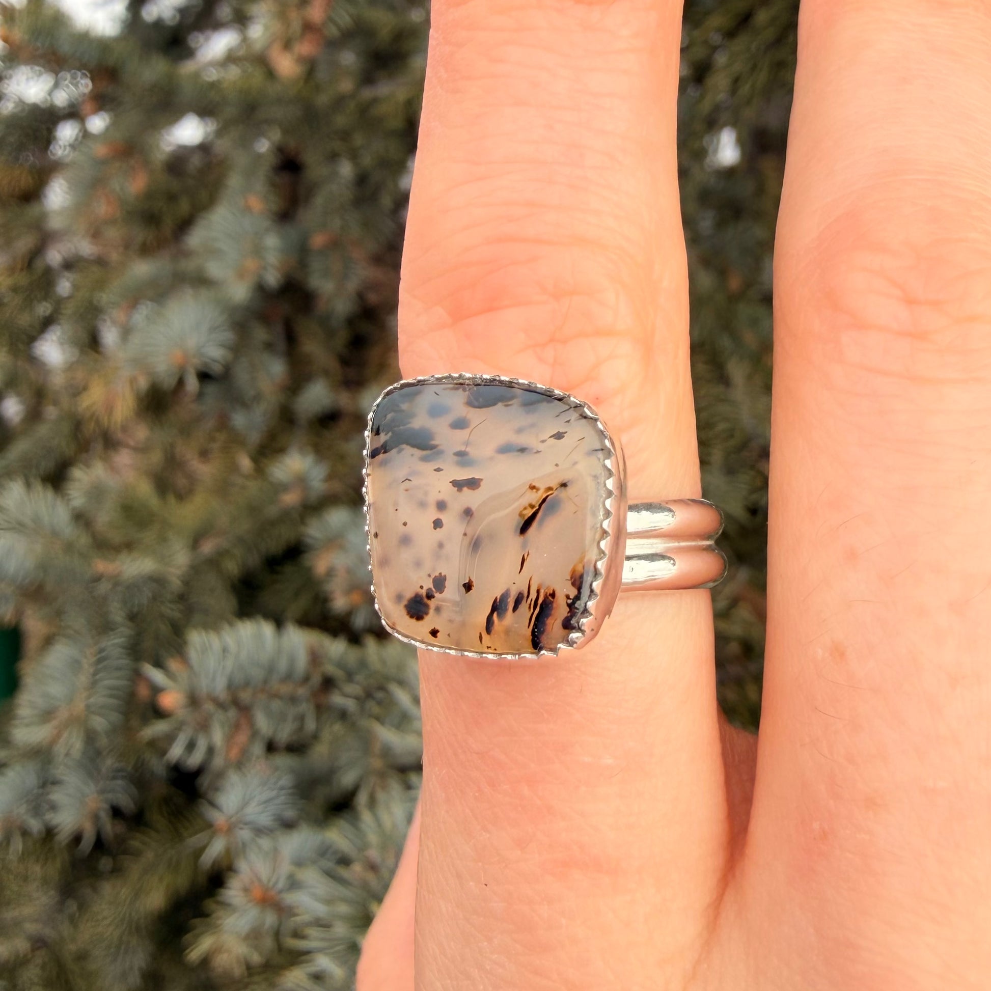 Hand wearing a ring with a speckled stone against a blurred natural background
