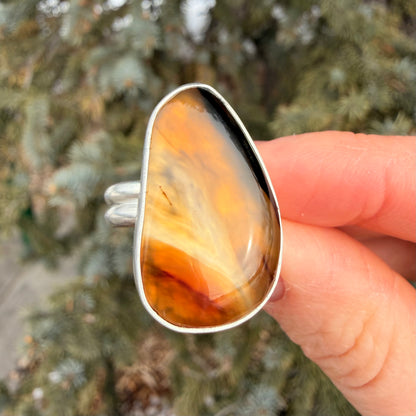 Hand holding a ring with a large, orange-brown stone against a blurred natural background