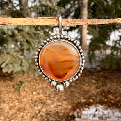 Silver pendant with amber-colored stone hanging outdoors