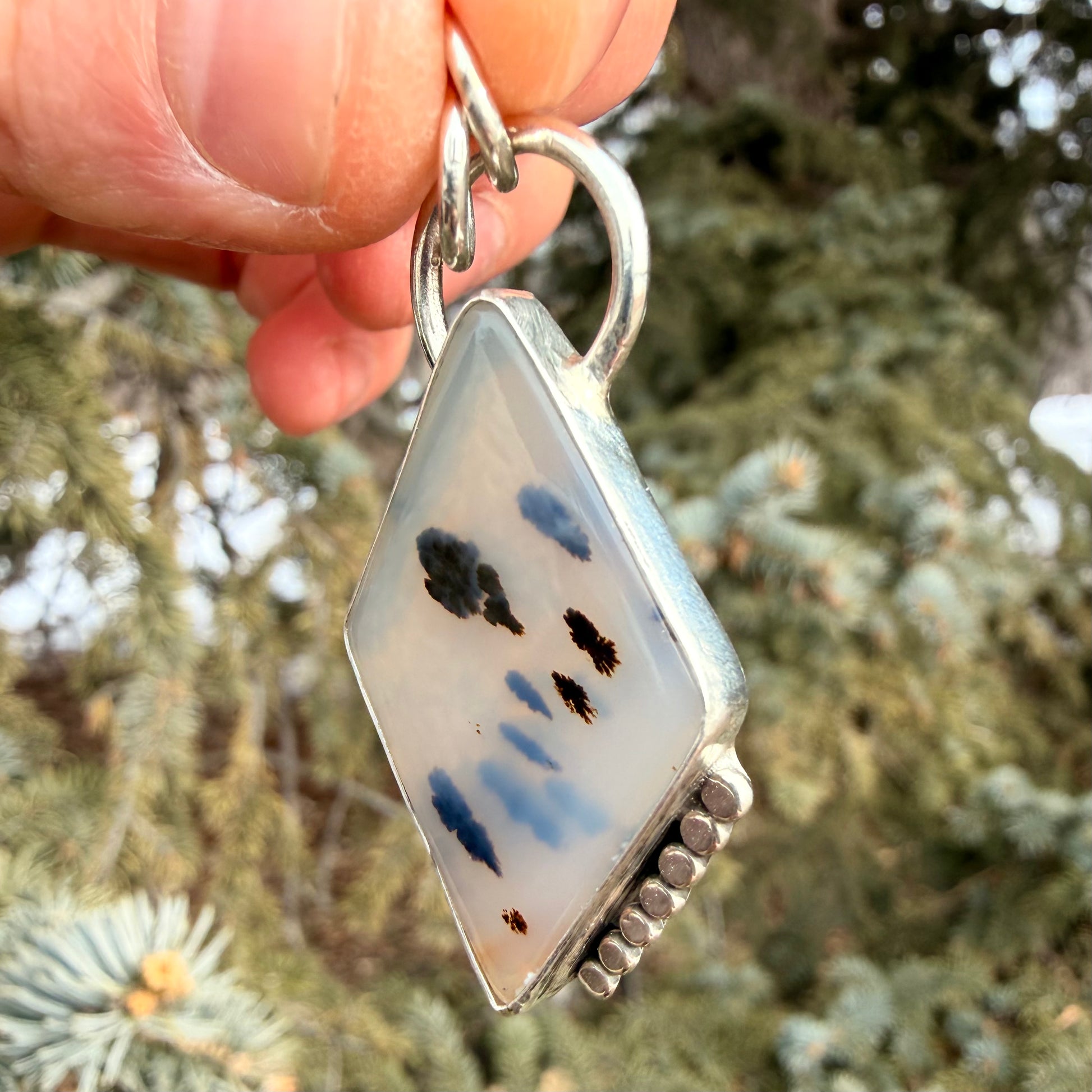 Decorative pendant with blue and black designs held against a blurred natural background