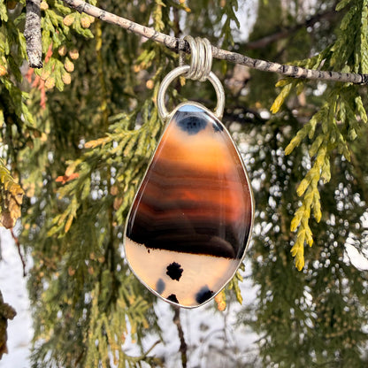 Teardrop-shaped agate pendant on a branch with green foliage in the background