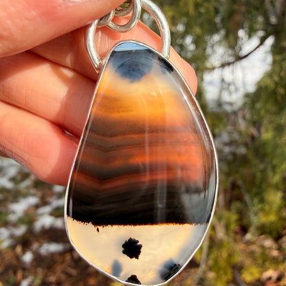 Teardrop-shaped agate pendant held by a hand with a blurred natural background