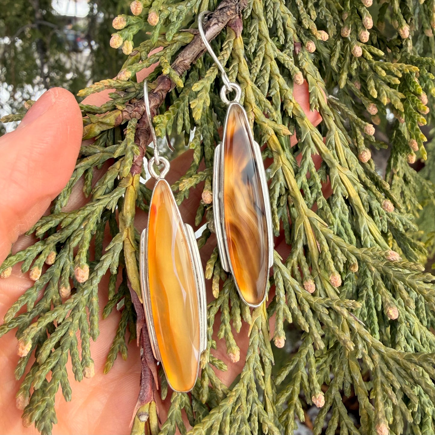Ornate earrings held against a green leafy background