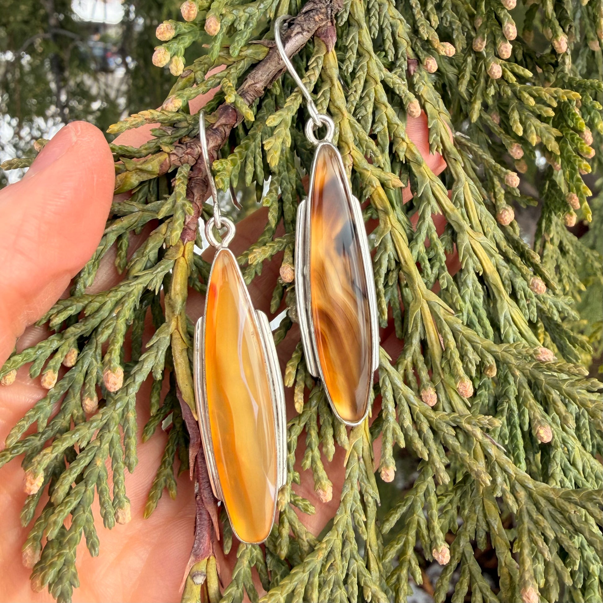 Ornate earrings held against a green leafy background