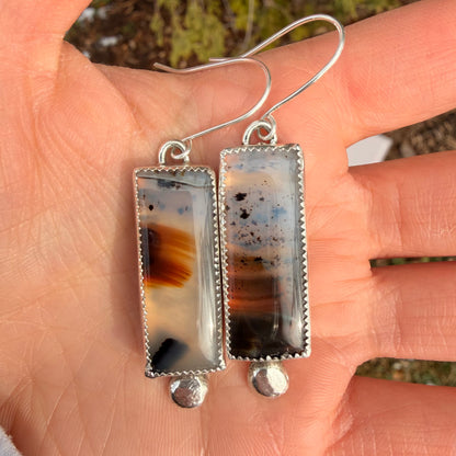 Rectangular agate earrings with silver setting held in a hand against a blurred natural background