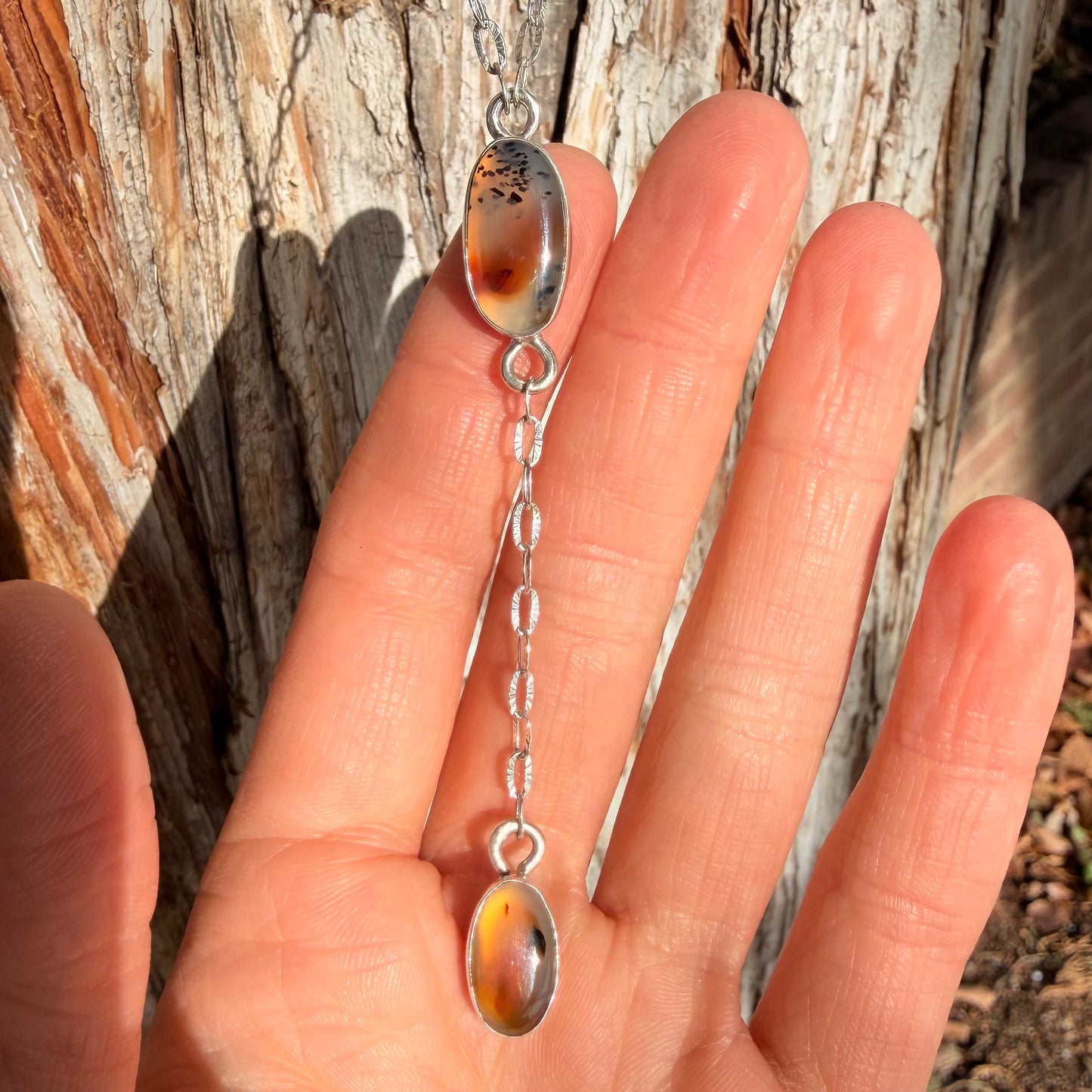 Hand holding a silver pendant with amber-colored stones against a wooden background