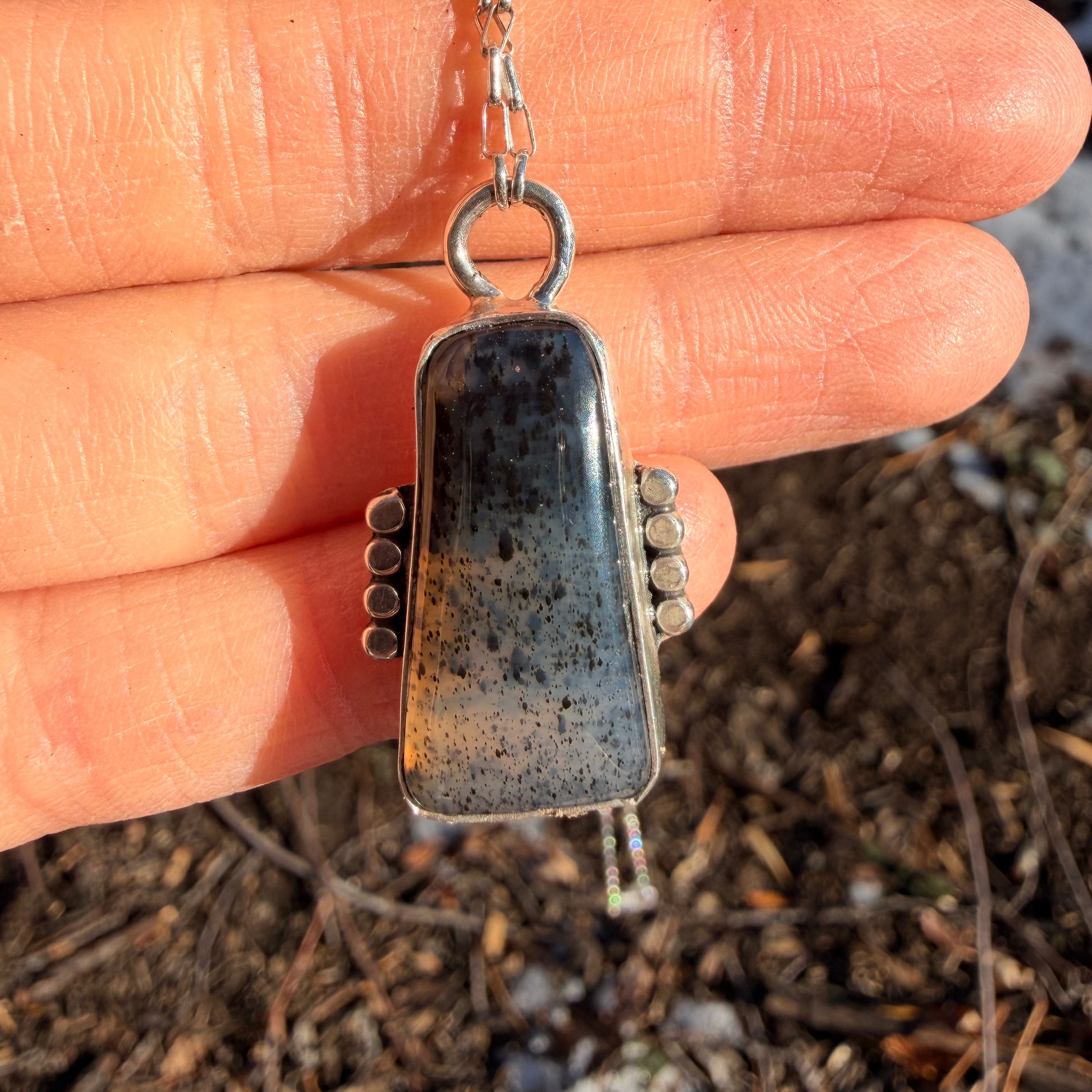 Silver pendant held between fingers with natural background