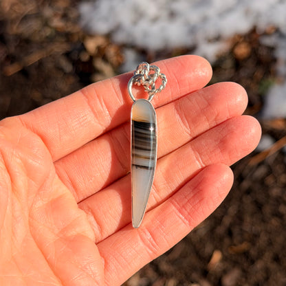 Hand holding a feather-shaped pendant with a blurred natural background